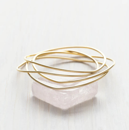 Stack of gold bangle bracelets sitting on a piece of rose quartz