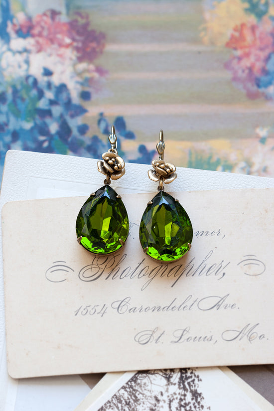 Green gem teardrop earrings with gold roses on stack of vintage postcards